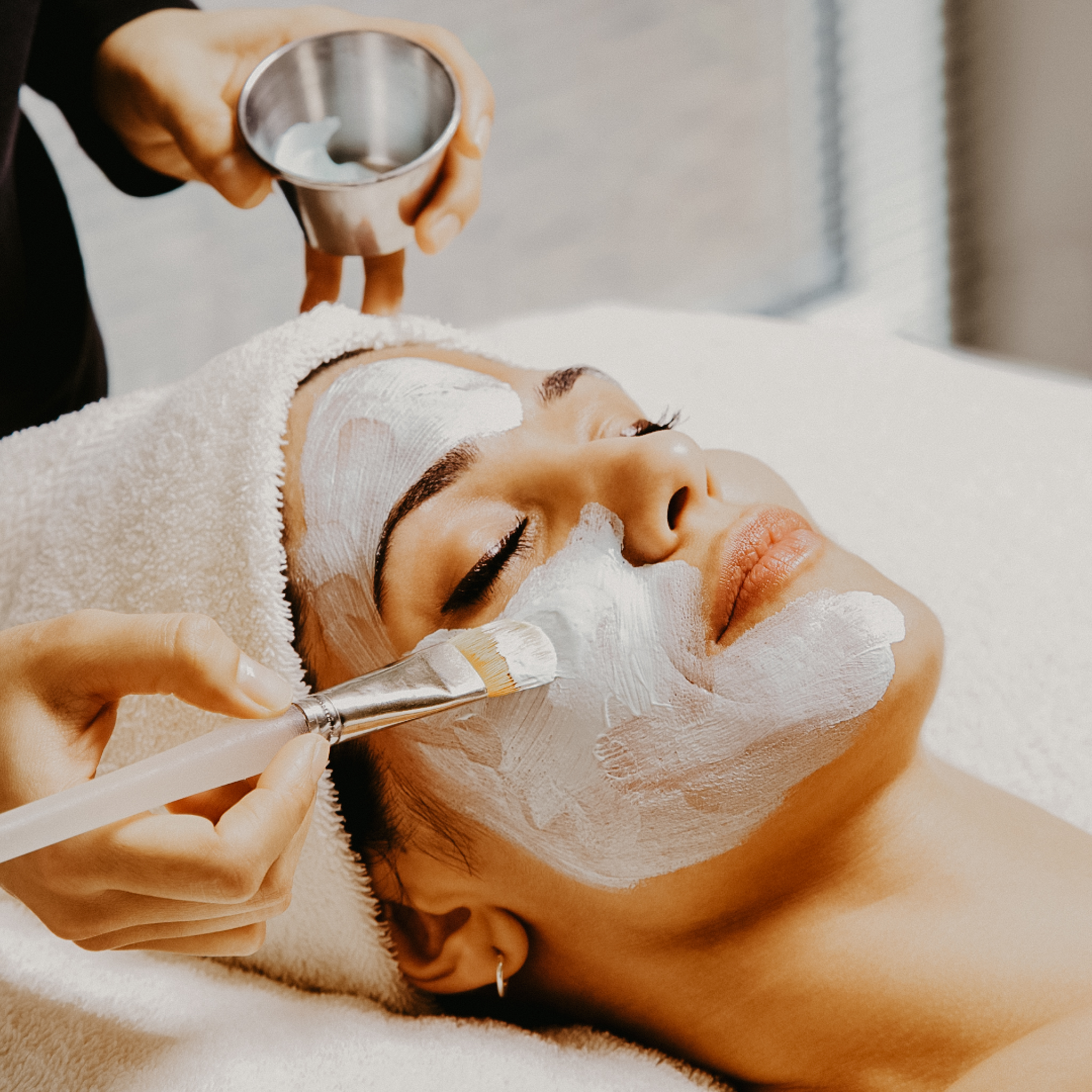 woman laying down with a white facial product being applied 