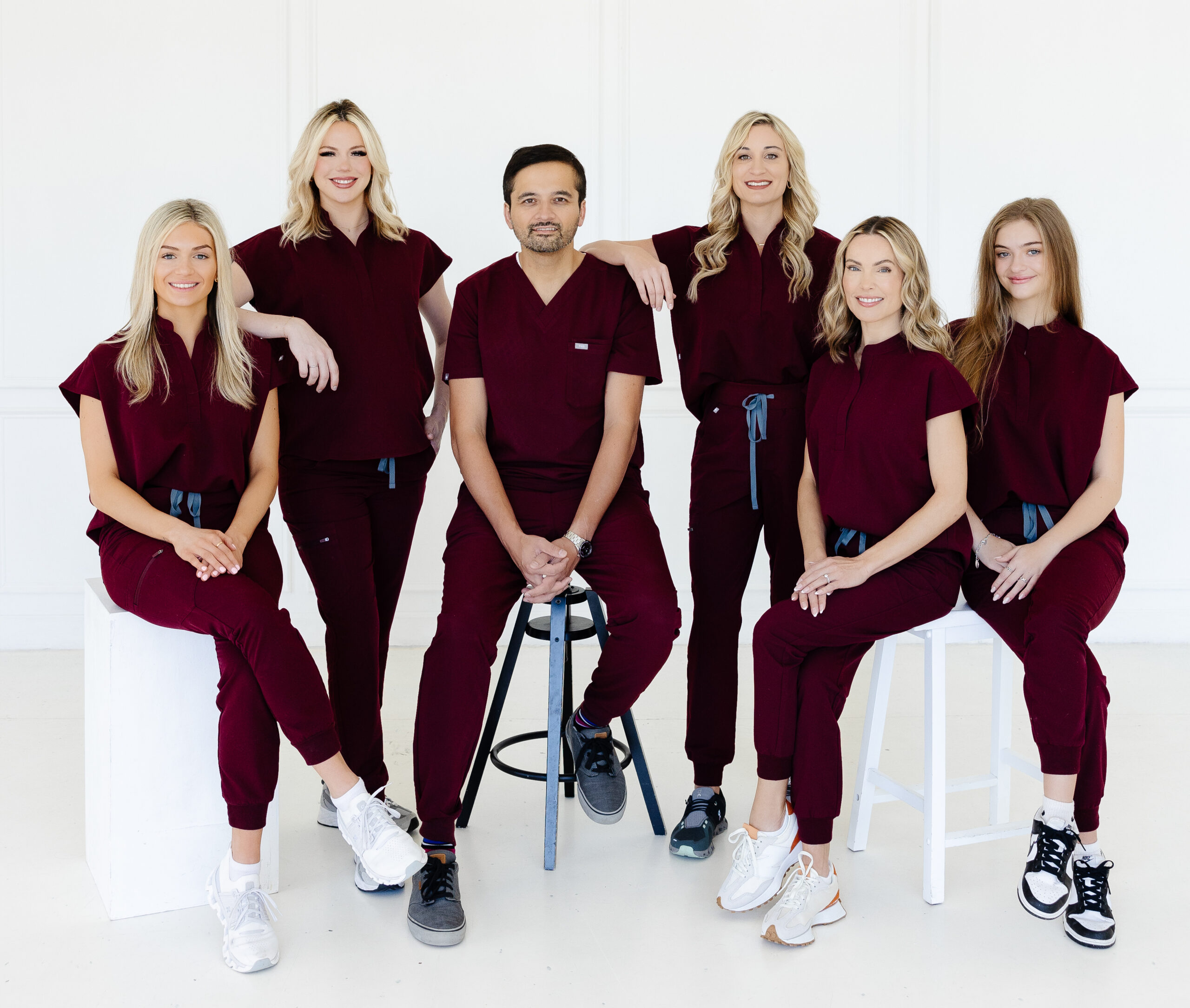 5 woman are standing around a man all wearing maroon scrubs and are showing the pride for all 5 star google med spa reviews southlake tx